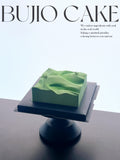 Load image into Gallery viewer, Mountain Wind mousse cake displayed on a sculptural pedestal.